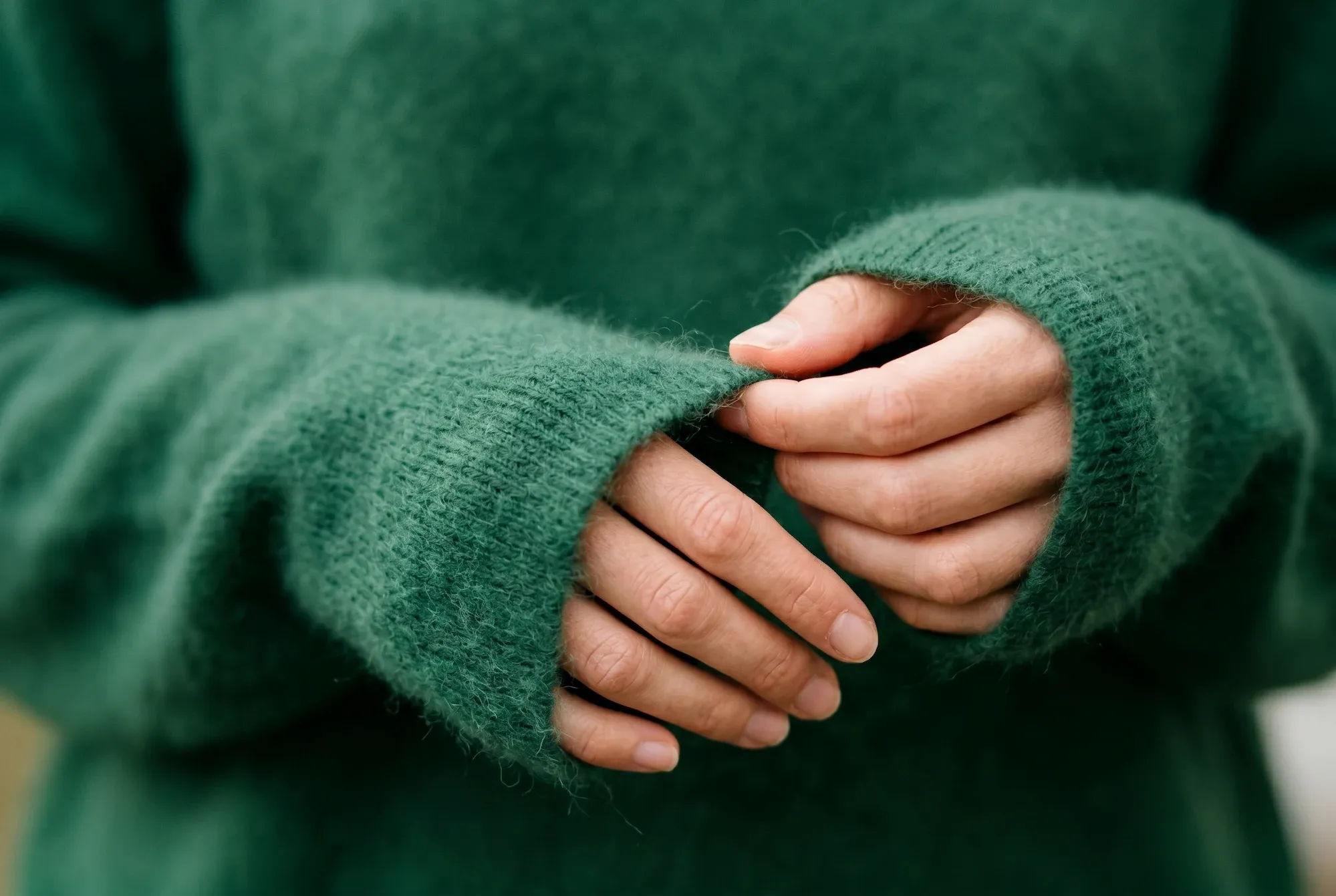 Hands touching a soft green knit sweater sleeve.